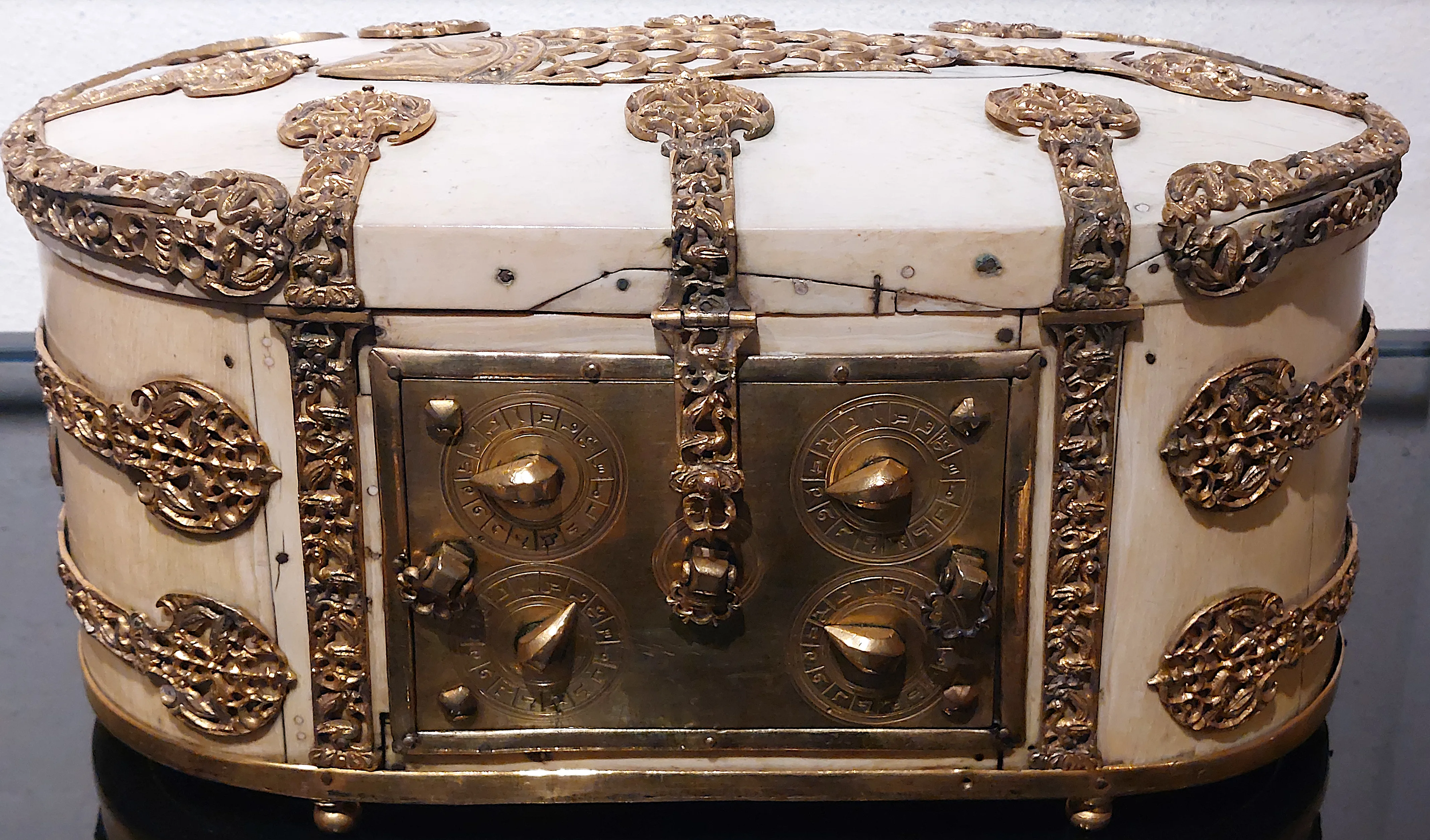 An oval ivory and gilt-brass casket, its lid and sides bound with pierced foliate metal mounts, and its front panel fitted with four rotating dials marked with Arabic letters around a central lock