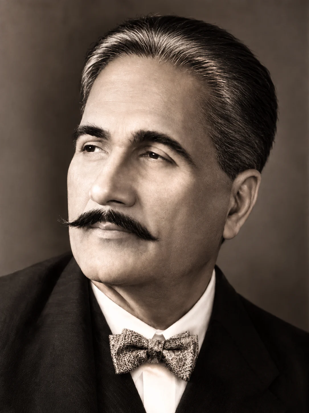 AI-generated impression: Sepia-toned head-and-shoulders portrait of a man with swept-back greying hair, heavy dark eyebrows and a full upturned dark moustache, looking slightly to one side, wearing a dark jacket, a white shirt and a patterned bow tie against a plain brown backdrop