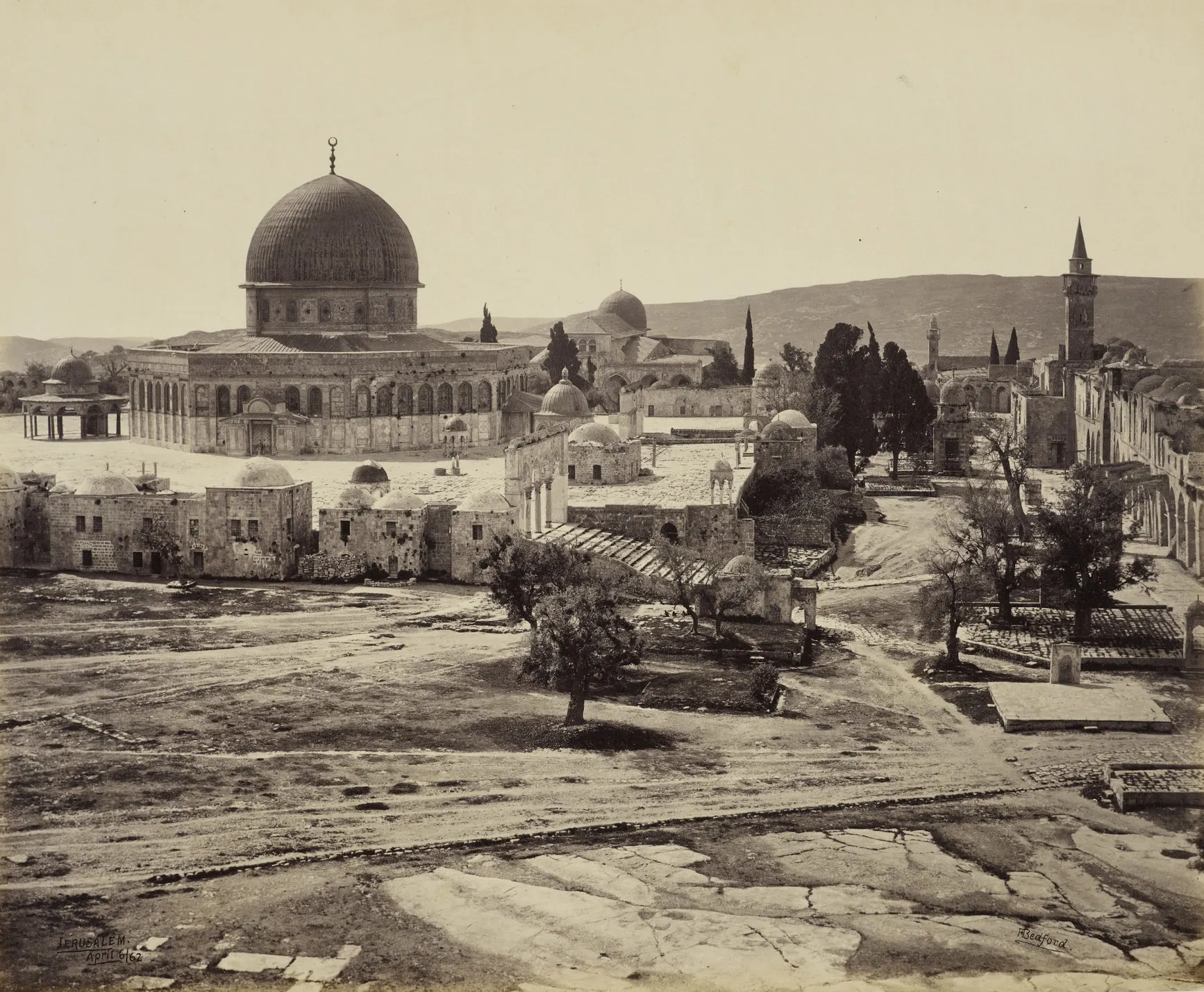 An early albumen photograph of a broad walled sanctuary platform, with a large domed octagonal building at the left, a second domed hall behind it, smaller domed structures and cypresses across the open ground, and an arcade running along the right