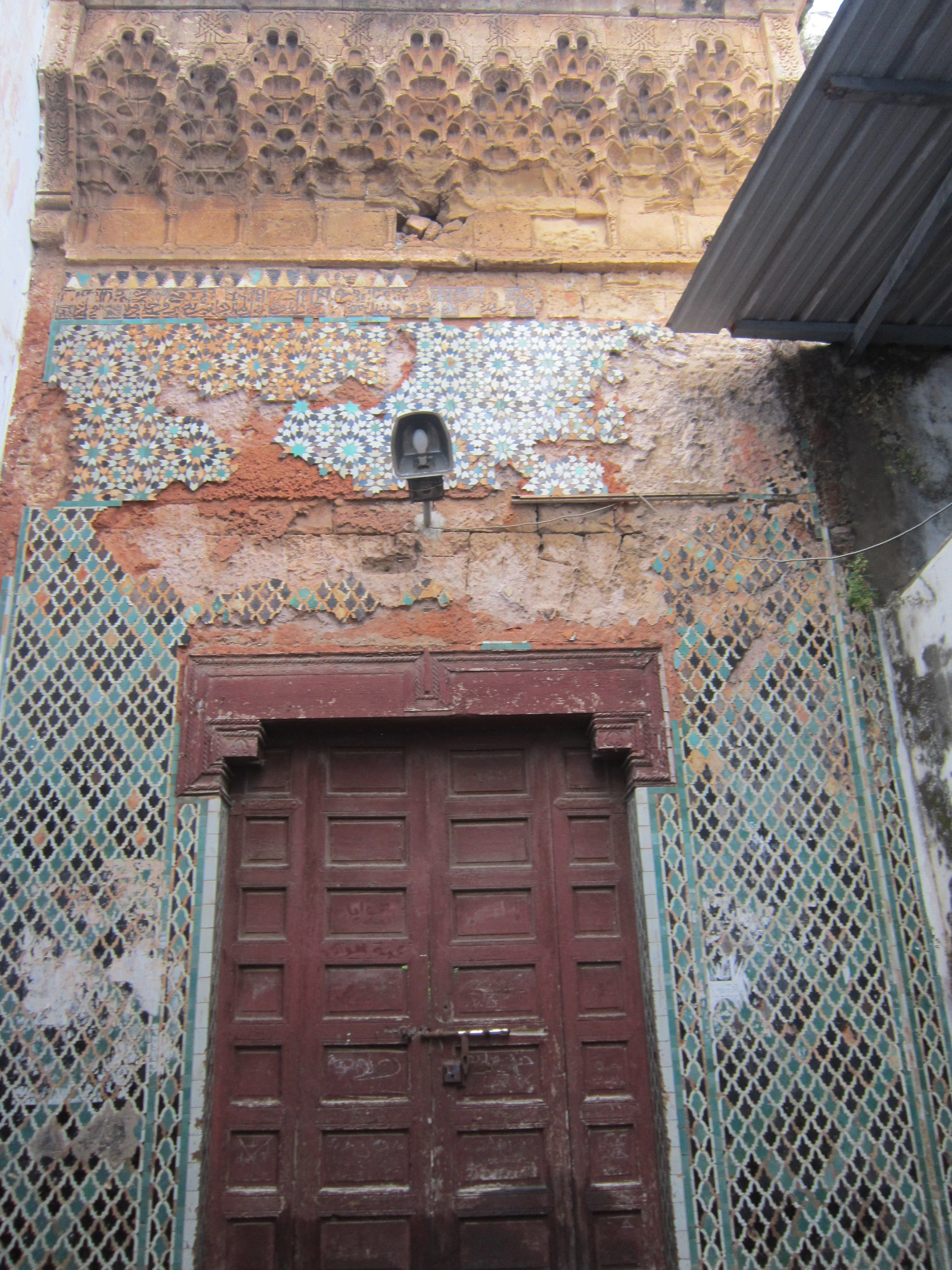 A weathered door with zellige tilework and carved muqarnas at the ancient hospital of Salé in Morocco, an example of the tradition of Islamic hospital architecture